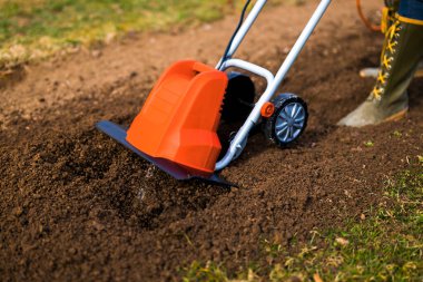 Bahçe yataklarını dikmek için hazırlayan kadın. Rotavator, bahçe dümeni, döner dümen ya da mini ekici. Tiller sıkıştırılmış toprağı parçalar, yapısını ve havasını geliştirir. Bahar bahçıvanlığı.