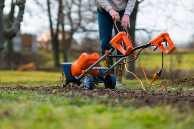 Bahçe yataklarını dikmek için hazırlayan kadın. Rotavator, bahçe dümeni, döner dümen ya da mini ekici. Tiller sıkıştırılmış toprağı parçalar, yapısını ve havasını geliştirir. Bahar bahçıvanlığı.