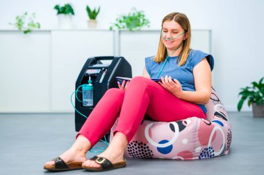 Oksijen terapisi, ek oksijen. Konsantratör makinesine bağlı burun kanülünden oksijen soluyan genç bir kadın.. 