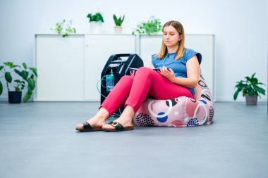 Oksijen terapisi, ek oksijen. Konsantratör makinesine bağlı burun kanülünden oksijen soluyan genç bir kadın.. 