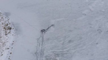 Kışın buzla kaplı nehirde balık tutan bir balıkçının hava görüntüleri.