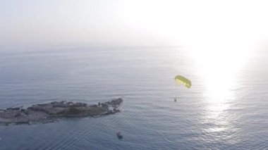 Gün batımında mavi denizin üzerinde sarı bir paraşüt üzerinde bir teknenin arkasında.
