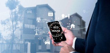 Modern eco-friendly house with windmill and solar panels. Sustainable smart home and energy-saving concept. The technology icon on a mobile phone and a house background