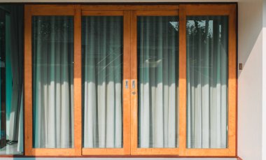 Kapı ahşap ve camdan yapılmış. İçinde gri-yeşil bir perde var. Camın yarısını geçince, güneş görünüyor. Oturma odasının içinde.