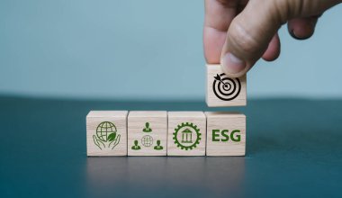 Çevresel, sosyal ve yönetim ESG olarak bilinir. Sürdürülebilir bir firma yaratmak. Bir ESG simgesi ve diğer ESG simgelerine ayarlanmış parlak bir arka planda, bir el ahşap küpleri tutuyor.