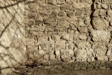 Yüzeyin üzerine doğal ışık saçan gölgeli kayalardan oluşan desenli taş bir duvar..