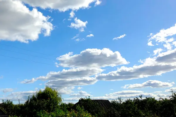 Pofuduk beyaz bulutlar parlak mavi bir gökyüzünde süzülür, huzurlu kırsalın yemyeşil yemyeşil gölgelerine gölge düşürür..