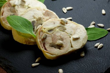 Dilimlenmiş et rulosu, taze ıspanak yaprakları ve ayçiçeği tohumlarıyla süslenmiş siyah bir seramik tahtada güzelce sunuluyor..