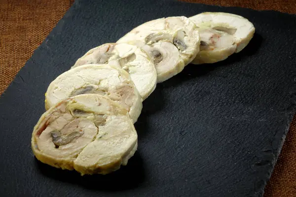 Taze ıspanak yaprakları ve parlak siyah bir tahtanın üzerinde ayçekirdeği ile süslenmiş, dilimlenmiş güzel bir rulo et..