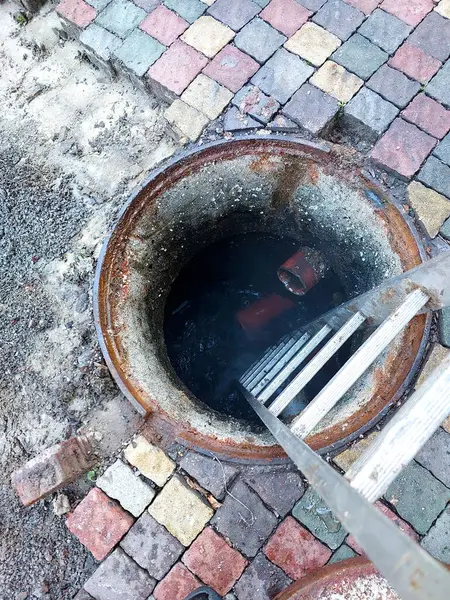 Çakıl taşı yüzeyi çöktükten sonra bir kanalizasyon kuyusu tamir ediliyor. Bu da içeride derin bir çukur ve su birikimini ortaya çıkarıyor..