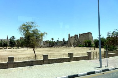 The grandeur of Luxor Temple is showcased with its impressive pylon gate and remnants of ancient statues, surrounded by a scenic landscape under clear skies.