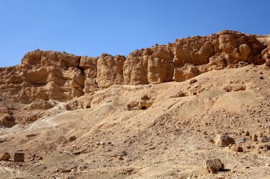 Kurak arazide, Queens Vadisi 'nin yüksek dağları tarafından berrak mavi gökyüzünün altında çerçevelenmiş Hatshepsut' un Morg Tapınağı kalıntıları yer alıyor..