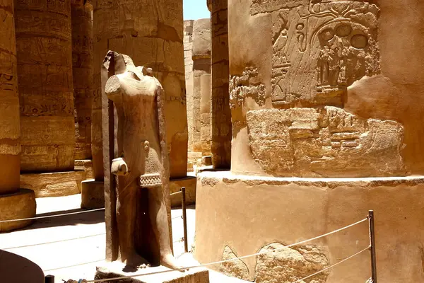 stock image The ruins of the Karnak temple complex showcase a massive statue, surrounded by intricately carved columns adorned with hieroglyphs, reflecting the grandeur of ancient Egypt.