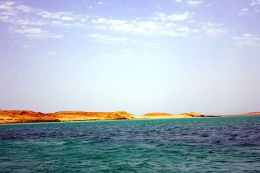 Denizin berrak suları, sakin mavi bir gökyüzü altında kumlu plajlar ve kayalık oluşumlarla süslenmiş pitoresk bir manzarayı gözler önüne sererek, Hurghada kıyılarına nazikçe uzanır..