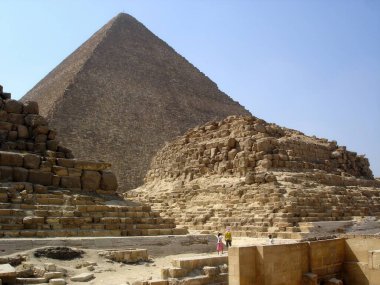 Giza Piramitleri Kahire yakınlarındaki çölde görkemli bir şekilde yükselirler ve antik mimariyi sergilerler. Ziyaretçiler parlak bir güneşin altında tarihi yapıların arasında geziniyorlar..