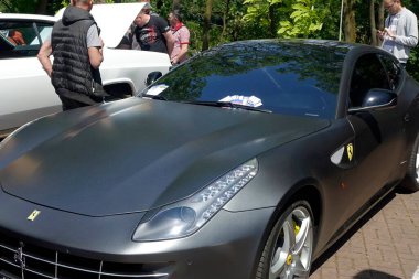 Lviv, Ukrayna - 1 Haziran 2023 Matte-gray Ferrari FF spor arabası, sohbete daldı ve sıcak öğleden sonranın tadını çıkardı. Ağaçlar aracın tasarımı ve özelliklerine hayran oldukları için gölgelik sağlar.