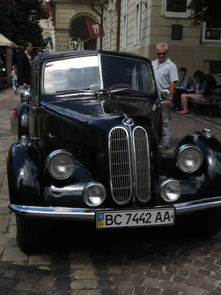 Lviv, Ukrayna - 20 Temmuz 2013 Pürüzsüz siyah bir BMW 335 Cabriolet eski model araba kaldırım taşı bir caddede duruyor, bir adam onu incelerken. Büyüleyici mimari, güneşli bir öğleden sonra bir Avrupa kasabasında sahneyi çevrelemektedir..