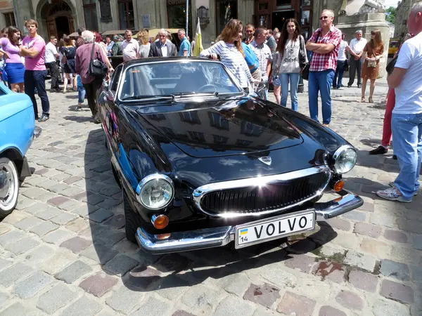 stock image Lviv, Ukraine - June 28, 2014 A classic black Volvo P1800 E attracts attention during. People admire the car as they socialize on a sunny day in a bustling town.