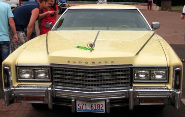 Lviv, Ukraine - June 14, 2015 A classic yellow Cadillac Eldorado stands proudly at a car show. Enthusiasts gather around, discussing its features and admiring its vintage charm on a sunny afternoon. clipart