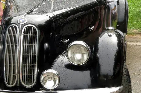 stock image Lviv, Ukraine - June 14, 2015 A vintage black car BMW 335 Cabriolet attracts attention at a park event, with a casually dressed man standing beside it, enjoying the atmosphere