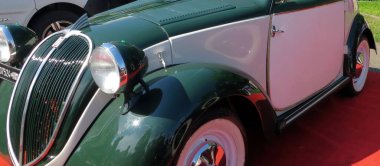 Lviv, Ukraine - June 5, 2016 A charming two-tone vintage car FIAT Topolino is showcased on a red carpet at a sunny outdoor event. Retro design, attracts attention amidst lush greenery