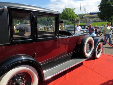 Lviv, Ukrayna - 5 Haziran 2016 1930 'larda bir halk etkinliğinde beyaz duvar lastikli klasik bir araba kırmızı halıda belirgin bir şekilde sergilendi. Katılımcılar açık mavi gökyüzünün altındaki araca hayran.