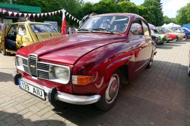 Lviv, Ukraine - June 6, 2017 A classic red car SAAB 96 V4 is displayed at a vibrant vintage auto exhibition in a park. Surrounding vehicles and festive decorations create a lively atmosphere clipart