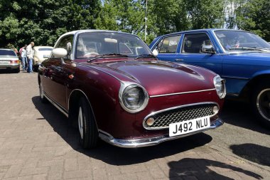 Lviv, Ukrayna - 1 Haziran 2023 güneşli bir günde diğer klasik araçların arasına beyaz çatılı bordo renkli bir Nissan Figaro park edilir. Katılımcılar araba toplantısının keyfini çıkarıyorlar.