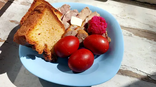 Canlı bir Paskalya tabağında kırmızı yumurtalar, dilimler, renkli yiyecekler ve taze ekmek sergileniyor. Mükemmel düzenlenmiş, bayramın şenlikli ruhunu yansıtıyor..