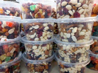 Çeşit çeşit fındık ve kurutulmuş meyvelerle dolu renkli plastik kaplar kalabalık bir pazarda düzgün bir şekilde istiflenir ve müşterileri sağlıklı atıştırmalıkların tadına bakmaya davet eder..