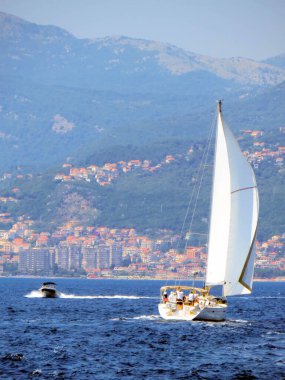 Karadağ 'ın Herceg Novi kentinde Boka Kotorska' nın sakin sularında kayan bir yelkenli yatı, muhteşem dağ manzarası ve Karadağ 'ın kıyı köyleri yer alıyor.