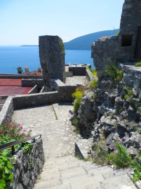 Ziyaretçiler, Karadağ 'ın Herceg Novi kentindeki açık ve güneşli bir günde Kotor Körfezi' nin çarpıcı manzarasının keyfini çıkararak tarihi Kanli Kula Kalesi 'nde geziniyorlar..