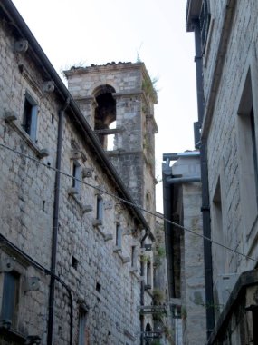 Kotors 'un eski kasabasında dolaş, yıpranmış taş binalar zengin tarihi sergiliyor dar sokakları gözetleyen bir çan kulesinin yanında.