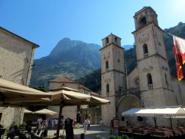 Kotor, Karadağ - 20 Temmuz 2014 Ziyaretçiler, güneşli bir günde arka planda yükselen güzel dağlarla Karadağ 'ın Kotor kentindeki tarihi Aziz Tryphon Katedrali' nin etrafında toplandılar..