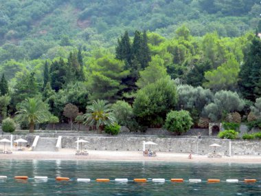 Sveti Stefan, Karadağ - 21 Temmuz 2014 Ziyaretçileri, Karadağ 'daki Sveti Stefan plajında sakin bir günün keyfini çıkarırken, berrak sular ve dingin ada tatil beldesi ortamını çevreleyen canlı yeşillikler.