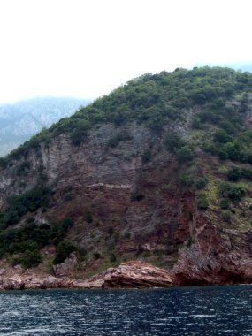 Montenegros kayalık kıyıları, Adriyatik Denizi boyunca sakin bir manzara yaratan çarpıcı uçurumlar ve yoğun yeşilliklere sahiptir. Sakin sular dramatik araziyi yansıtır..