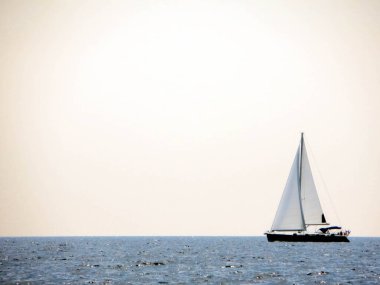 Bir yelken yatı sakin denizde zarifçe hareket eder, beyaz yelkenleri temiz bir gökyüzünün altında esintiye yakalanır..