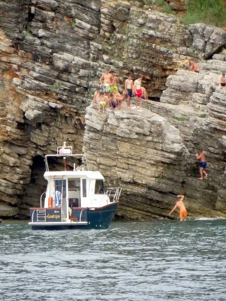 Budva, Karadağ - 21 Temmuz 2014 Maceracılar yakınlarda bir tekne demirlerken Sveti Nikola Adası 'nın kayalıklarından suya atladılar. Güneş tarafından öpülen kayalar ve kristal berrak sular