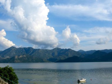 Küçük bir tekne Skadar Gölü 'nün sakin sularında sessizce sürüklenir. Etrafı görkemli dağlar ve tüylü beyaz bulutlarla çevrilidir. Doğa güzelliği kalbi cezbeder..