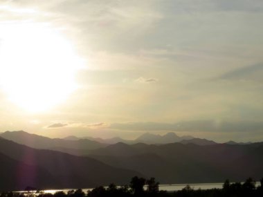 Alacakaranlıkta, Karadağ 'daki Skadar Gölü' nün üzerinde yumuşak dalgaların kıyıya vurduğu yerde gökyüzü hafifçe parlıyor ve uzaktaki sakin dağ siluetlerini çerçeveliyor..