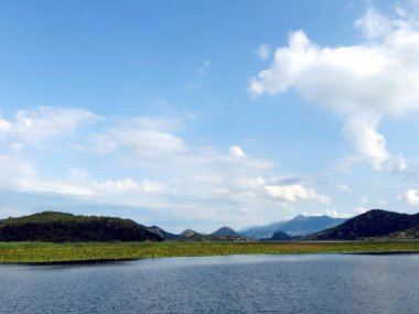 Berrak mavi gökyüzü Skadar Gölü 'nün sakin sularını yansıtıyor. Bereketli yeşillik nefes kesen manzarayı sarıp sarmalıyor. Gezginlere huzur ve macera sunuyor..