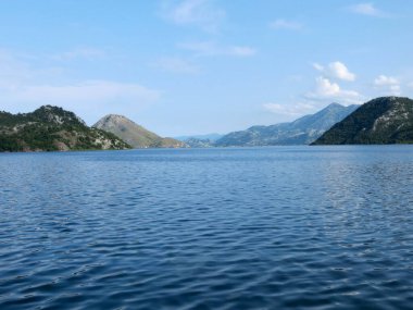 Skadar Gölü 'nün nefes kesici manzaraları berrak mavi gökyüzünün altındaki bereketli dağlar tarafından çerçevelenmiştir. Gezginleri sakin cazibesini ve doğal ihtişamını yaşamaya davet eder..
