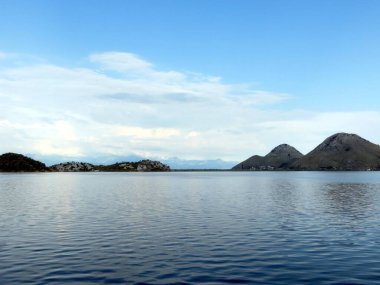 Skadar Gölleri 'nin el değmemiş suları, dağları çevreleyen huzurlu bir gökyüzünü yansıtırken, Karadağ' da sükunet isteyen doğa severler için çarpıcı bir zemin oluşturuyor.