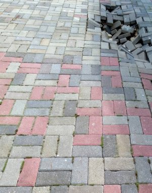 Kaldırımdaki çatlaklar, halka açık bir yolda düzensiz yüzeyler ortaya çıkarak bakım ve onarım ihtiyacını vurguluyor. Taşların arasında otlar büyüyor, bu da ihmalkarlığı gösteriyor..