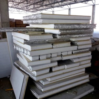 Çoklu sandviç paneli parçaları bir depoda üst üste yığılır, beyaz yüzeyleri ve katmanlı yapıları sergilenir. Yaklaşan inşaat projelerine hazırlıklılar..