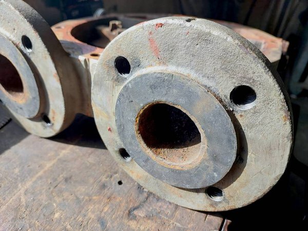 Close-up view of cast iron pump housing flanges, revealing surface texture and mounting holes, set on weathered wood in a workshop environment.