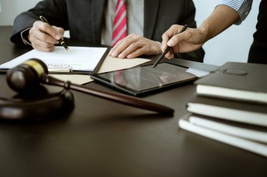 Avukat, asistan tabletini kullanarak tabloya ölçek ve tokmakla bilgi verirken yasal bir belge taslağı hazırlıyor.