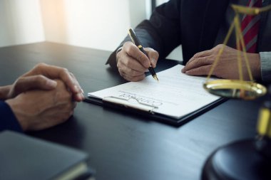 Avukat, müşterinin bilgilerini masada tartıyla ve tokmakla dinlerken yasal bir belge hazırlıyor.