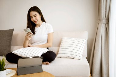 Kanepede oturan Asyalı kadın elinde akıllı bir cep telefonu tutarak dostça bir gülümsemeyle yana döndü..