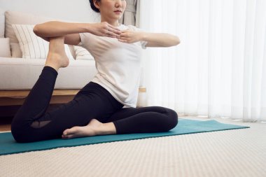 Yoga egzersizi yapan genç bir kadın evdeki kanepenin yanındaki minder üzerinde poz veriyor.